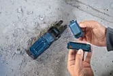 埃っぽいコンクリートの床の上で電動工具ベースのバッテリーを交換している人。