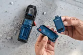 人が埃っぽいコンクリートの床の上の工具の隣にある青い電池ケースを開けています。