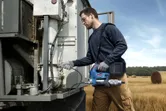 安全装備を身に着けた人が、畑で電動工具を使って農機具の整備をしている。