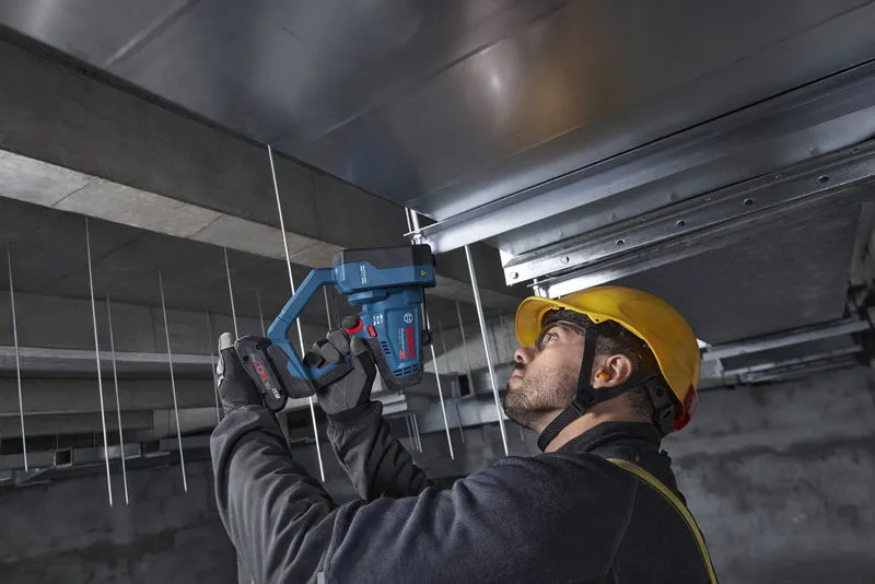 安全装置を装着した人が、天井のロッドにコードレスのネジ棒カッターを使用しています。.