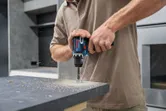 コードレス電動工具を使ってカウンタートップに穴を開けている人。