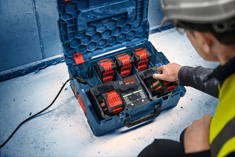 安全装備を身に着けた人が、作業現場でマルチバッテリー充電ステーションを操作しています。.