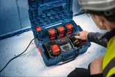 安全装備を身に着けた人が、作業現場でマルチバッテリー充電ステーションを操作しています。.