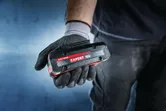 手袋をはめた手で持つBosch Expert 18V バッテリー。.