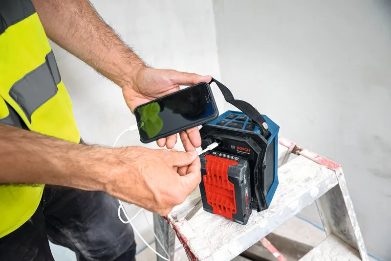 安全装備を身に着けた人が、はしごの上で携帯用電源を使って携帯電話を充電している。