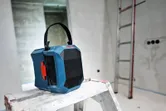 建設中の部屋にある脚立の上に、持ち運び用のハンドルが付いた現場用ポータブルラジオが置かれています。.