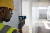 安全装備を身に着けた人がドア枠にレーザー測定器を当てています。