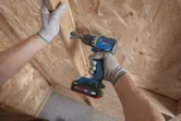 安全装備を身に着けた人が木製パネルにネジをドリルで打ち込んでいます。