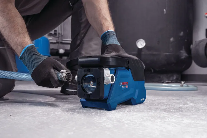 安全装備を身に着けた人がコンパクトな青いウォーターポンプにホースを接続しています。