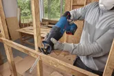 安全装置を装着した人がコードレスレシプロソーで木枠を切断しています。
