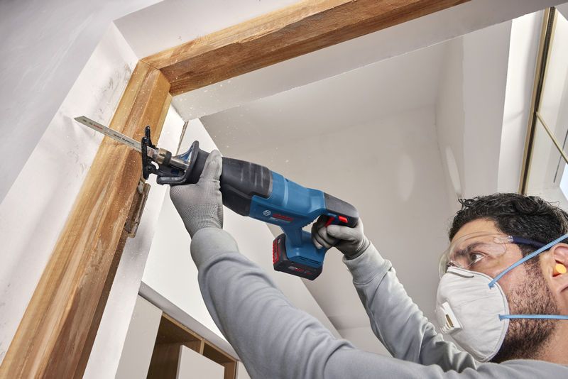 安全装置を装着した人がコードレスレシプロソーを使用してドア枠を切断しています。