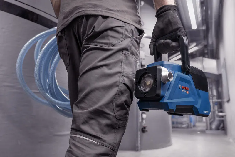 安全装備を身に着けた人が、産業現場で青いポータブル真空ポンプを運んでいます。