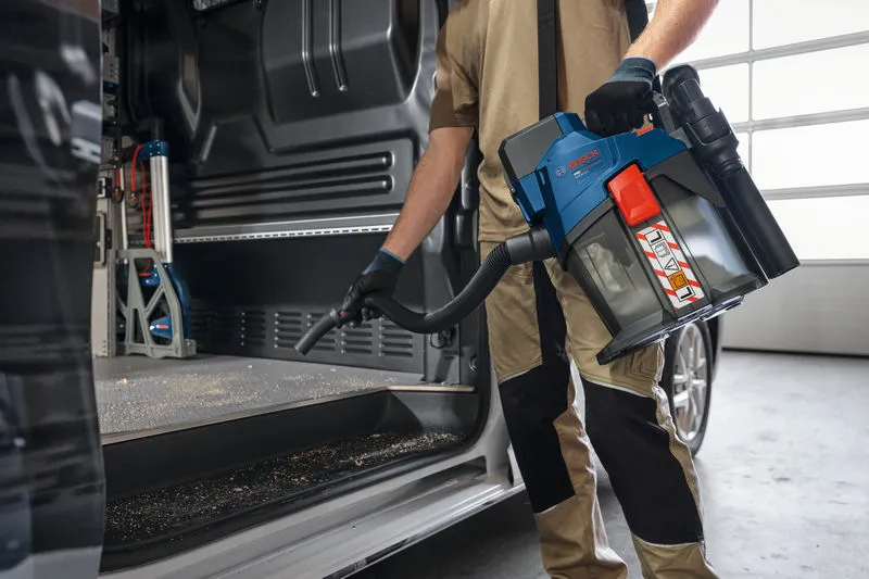 安全装備を身に着けた人が、コードレス集塵機を使用して車内を掃除しています。