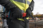 安全装備を身に着けた人が、建設現場でバックパックに取り付けられたベルトを調整している。