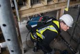 安全装備を身に着けた人が、電源バックパックを背負いながら工具を使用している。