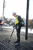 安全装置を装着した人が鉄筋グリッド上でコンクリートバイブレーターを使用しています。