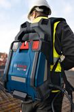 安全装備を身に着けた人が建設現場で青いバックパック型コンクリートバイブレーターを運んでいます。