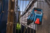 青と赤の電動工具が、屋外の金属製のワイヤーフェンスにもたれかかっている。