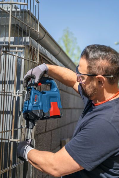 安全装備を身に着けた人が、電動工具を使って金属製のフェンスに穴を開けている。