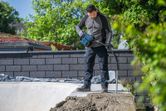 安全装備を身に着けた人が、屋外で電動工具を使ってコンクリートを締め固めている。