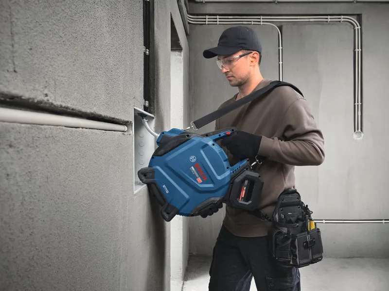 安全装備を身に着けた人が、壁に取り付けられたボックスに電気ケーブルを引き込んでいる。