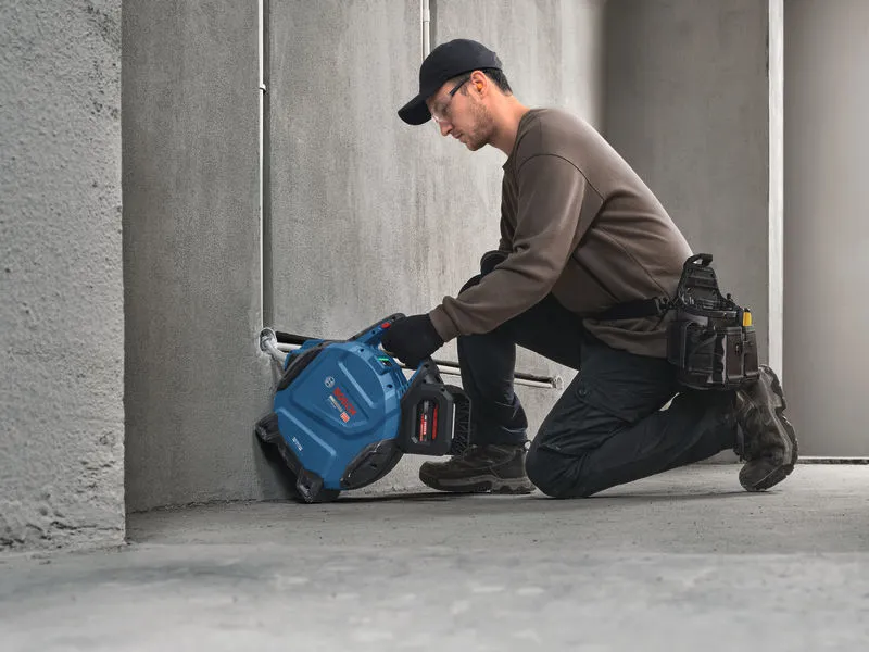 安全装備を身に着けた人が、電動工具を使ってコンクリートに溝を掘っている。