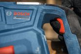 安全装備を身に着けた人物が、赤いトリガーが付いた青い電動工具のハンドルを握っている。