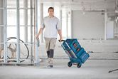 建設現場で、工具箱を積み重ねた折りたたみ式ハンドトラックを引いている人。