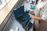 安全装置を装着した人が作業場でコードレスドリルを準備しています。