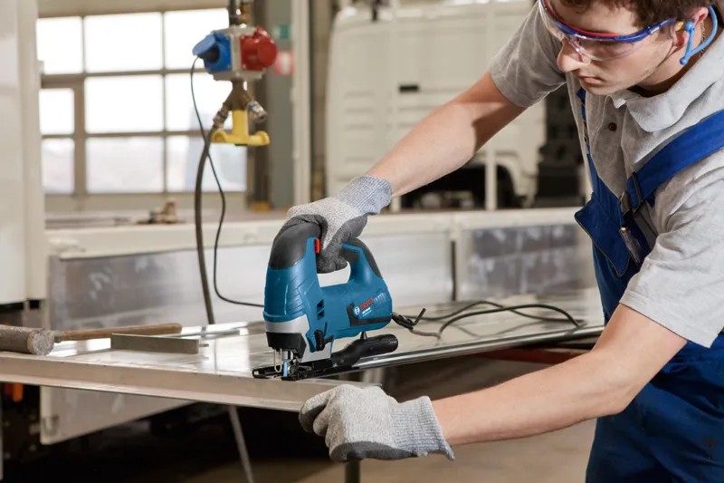 安全装置を装着した人がジグソーを使って金属板を切断しています。.