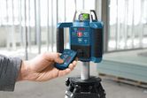 建設現場内で、人が三脚に取り付けたレーザー水準器を操作している。