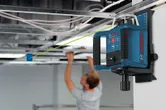 レーザー水平器が緑色の線を投影し、人が吊り天井を設置している。
