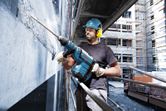 安全装備を身に着けた人が回転ハンマーを使用して建設現場でコンクリートを破壊しています。