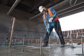安全装備を身に着けた人が回転ハンマーでコンクリートに穴を開けています。