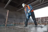 安全装備を身に着けた人が回転ハンマーでコンクリートに穴を開けています。.