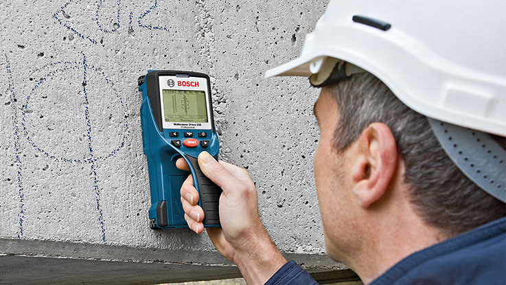 ボッシュの測定器を持つ作業員がコンクリート壁を測定している。